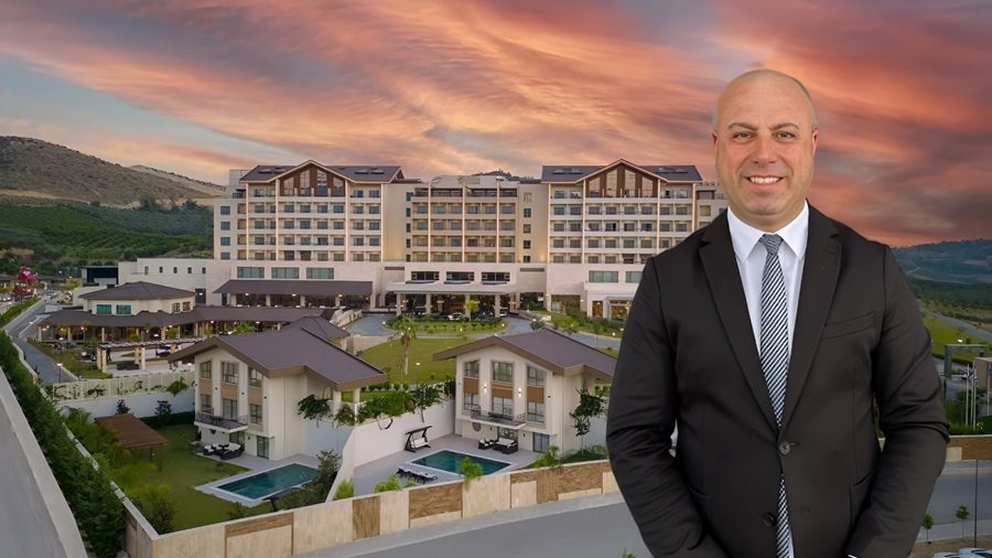 Businessman in a dark suit stands in front of a large resort hotel at sunset with pools and greenery in the foreground