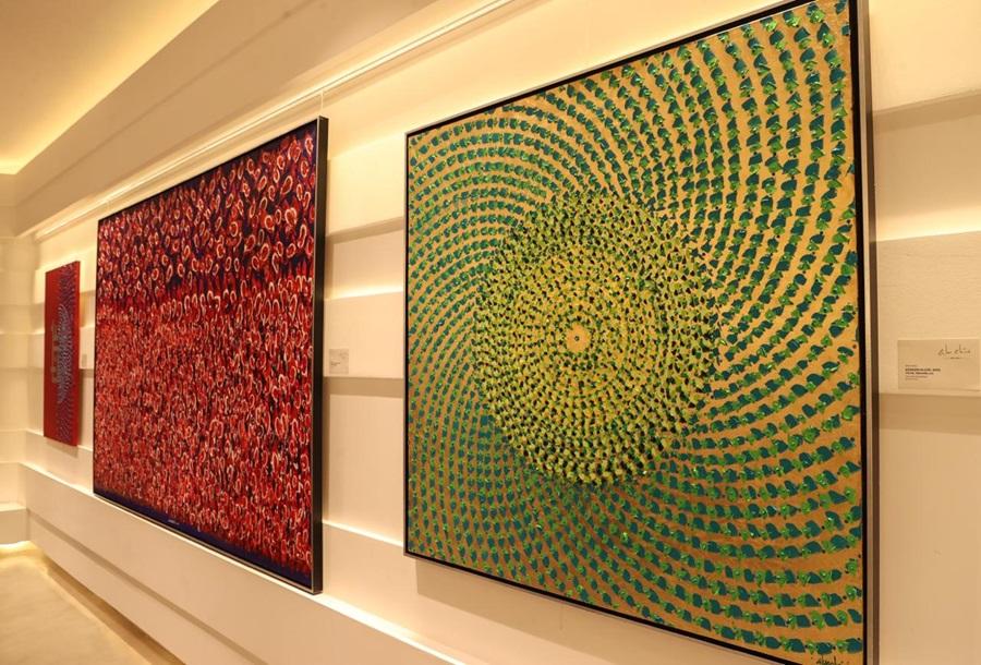 Gallery wall with two large abstract paintings: a red dotted pattern on the left and a green concentric-dot spiral on the right.
