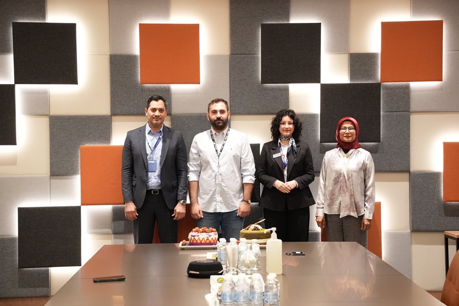 Four professionals pose for a photo behind a conference table with cakes and drinks, in a geometric wall backdrop.