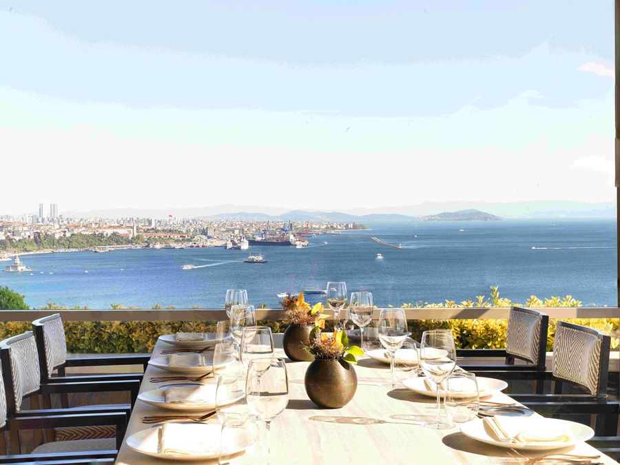 Table set for a meal with glassware and flowers, overlooking a harbor and blue sea.