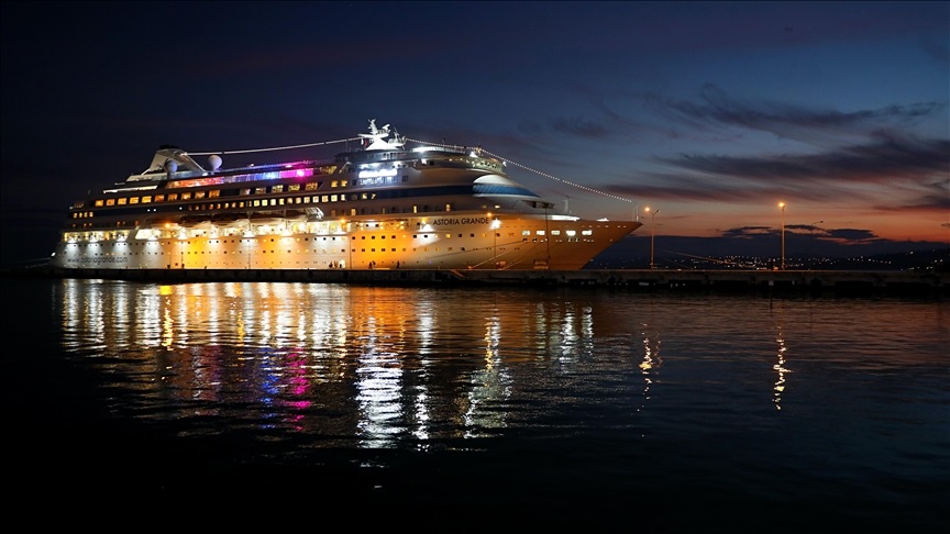 Cruise ship Astoria Grande docked at night with bright exterior lights and reflections on the water.