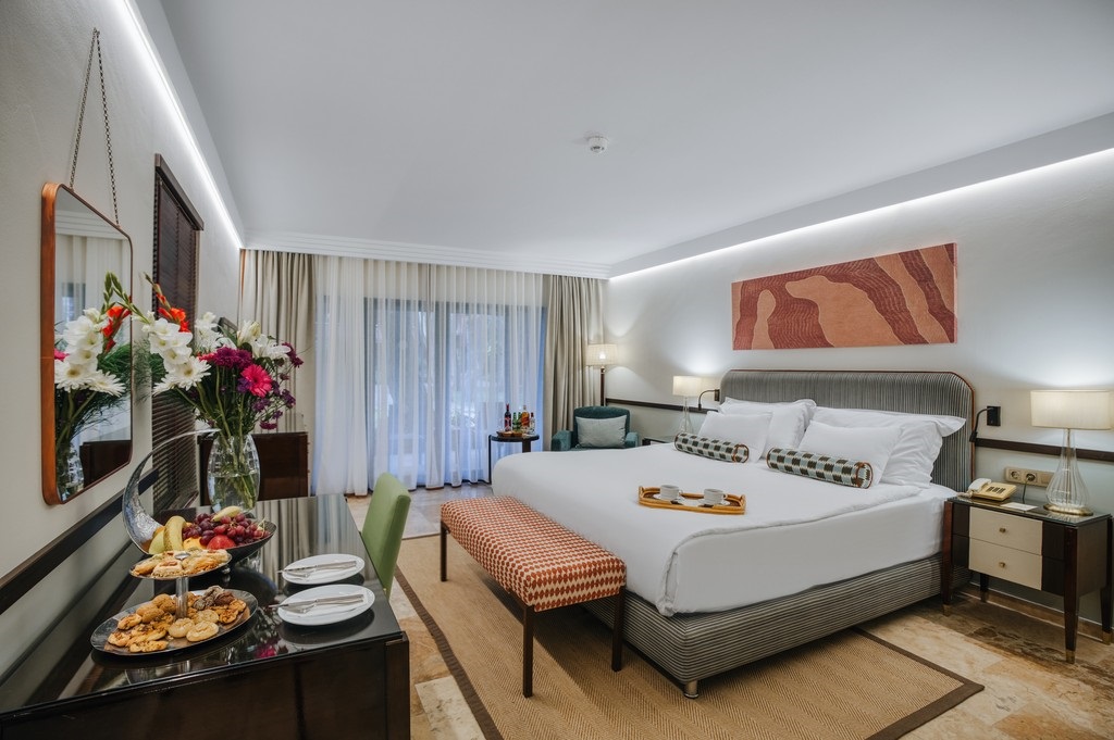 Luxurious hotel bedroom with a king bed, striped headboard, two nightstands, and soft lighting on either side.