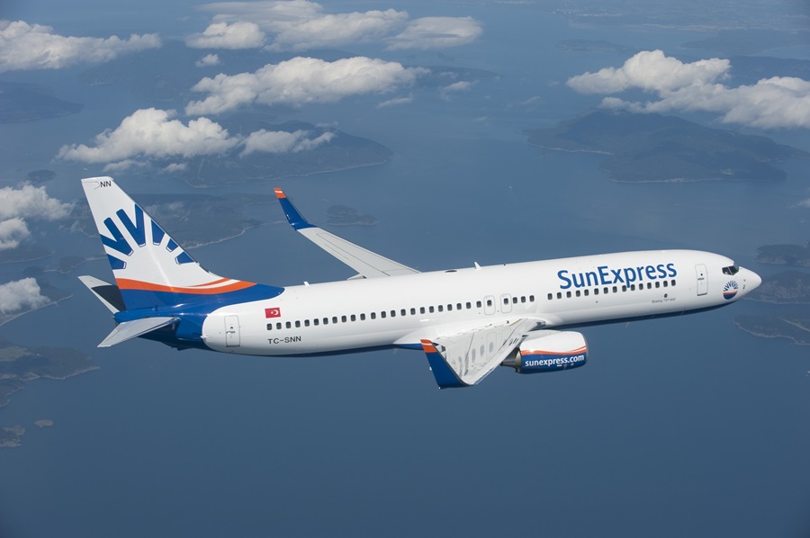 SunExpress passenger jet in flight over a blue sea with small islands below.