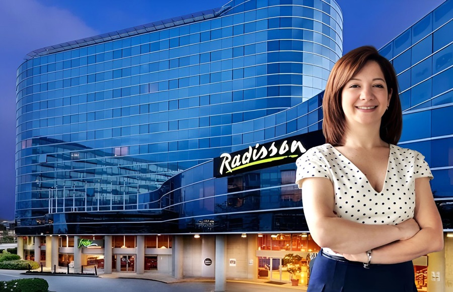 Smiling woman with folded arms standing in front of a blue glass Radisson hotel building.