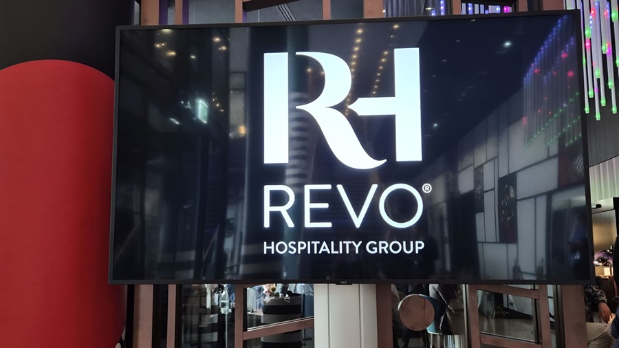 Large digital screen showing the REVO Hospitality Group logo in white on a dark background, inside a modern space.