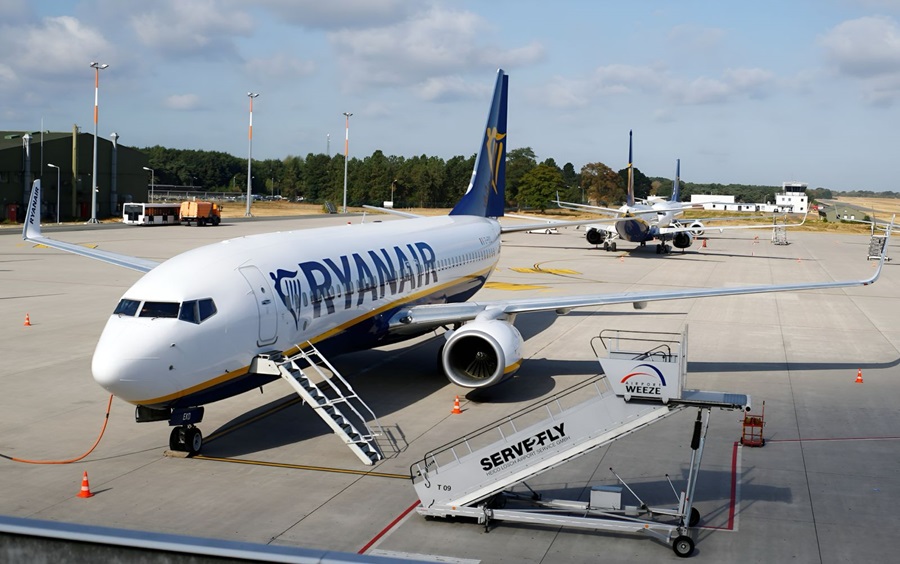 Ryanair airplane parked at the gate with mobile stairs attached for boarding on a sunny tarmac.