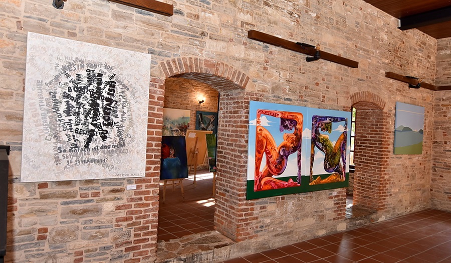 Brick-walled art gallery with arched doorways and paintings displayed along the walls.