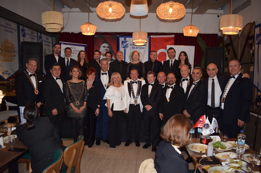 Group of guests in tuxedos and evening dresses posing for a formal group photo at a banquet hall/social event.