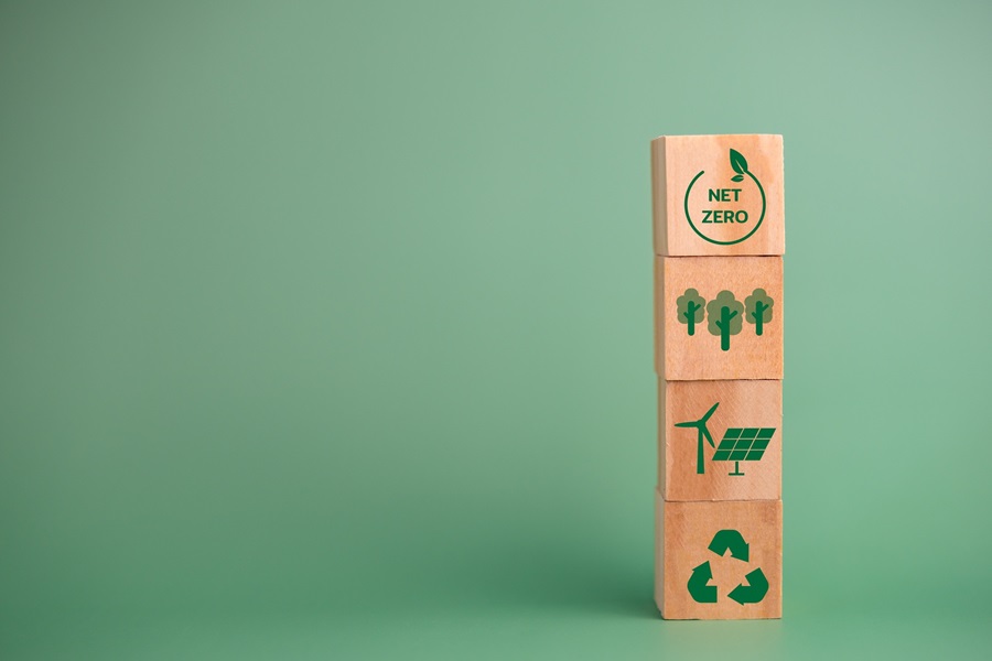 Stack of four wooden blocks with green eco icons—net zero, trees, wind and solar energy, and recycling—against a green backdrop.