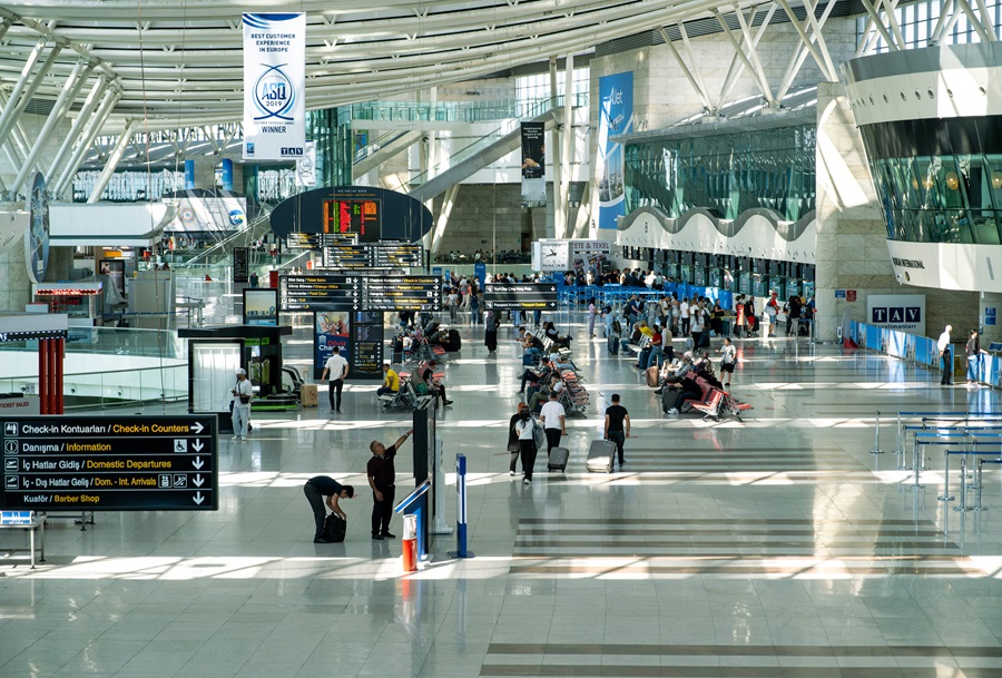 Busy airport terminal with check-in counters, digital boards, and travelers with luggage, sunlit and airy. (informative)