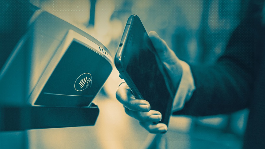 Person holding a smartphone near a contactless payment terminal to pay with NFC.