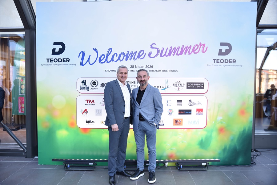 Two men in suits pose together in front of a large 'Welcome Summer' banner with sponsor logos at a formal event, date 28 Nisan 2026 visible in the background.