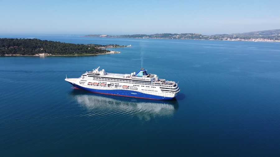 Large white cruise ship sailing in calm blue water near a coastline with green islands in the distance.