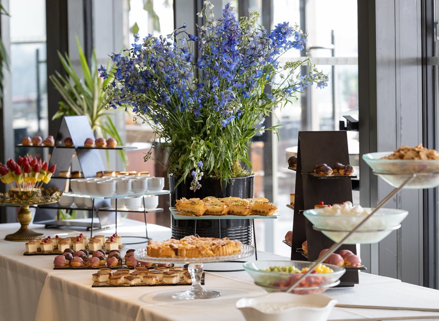 Elegant dessert table with a large blue floral centerpiece and assorted pastries on multi-tier stands.