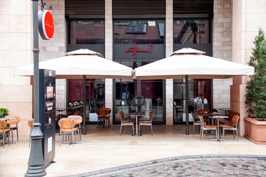 Outdoor cafe seating with white umbrellas in front of a storefront.