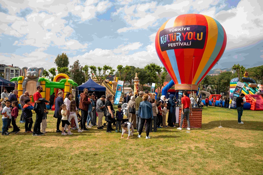 Crowd lines up at an outdoor Turkish cultural festival with inflatable attractions and a large striped hot-air balloon reading Türkiye Kültür Yolu Festivali.