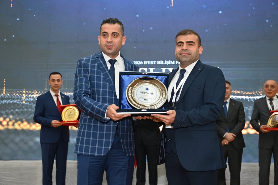 Two men in suits on a stage presenting a framed circular plaque at an awards ceremony, with others in the background