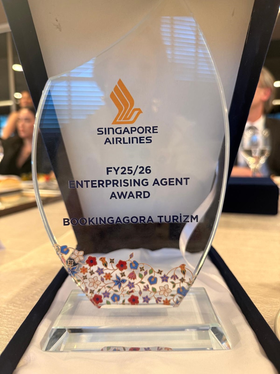 Glass Singapore Airlines award trophy reading 'FY25/26 Enterprising Agent Award' for Bookinggagora Turizm, with a floral base.