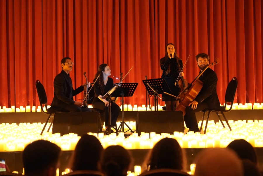 A four‑member string quartet on a stage with red curtains and many candles, performing for an audience.
