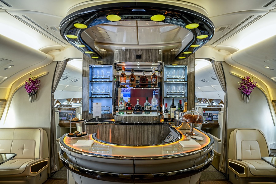 Circular bar inside a private jet, with illuminated liquor shelves, bottles, and cream leather seating along the cabin.