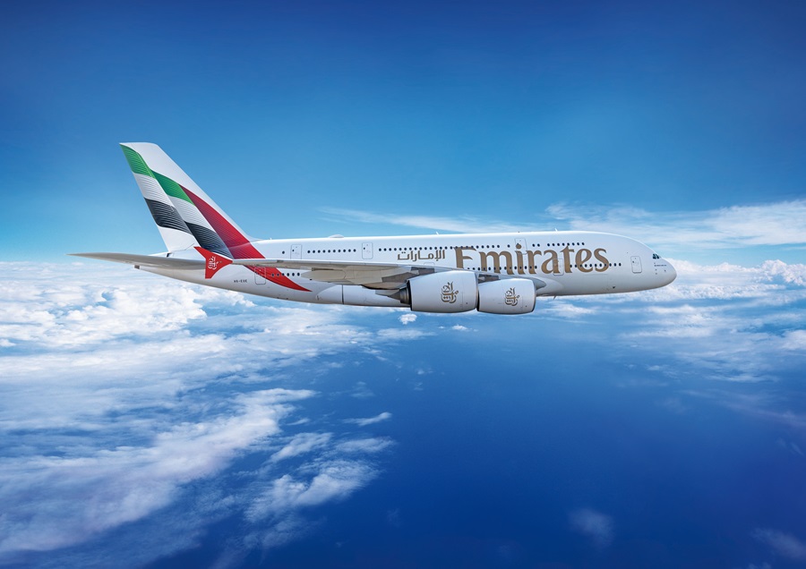 Emirates Airbus A380 in flight above clouds with a blue sky backdrop.