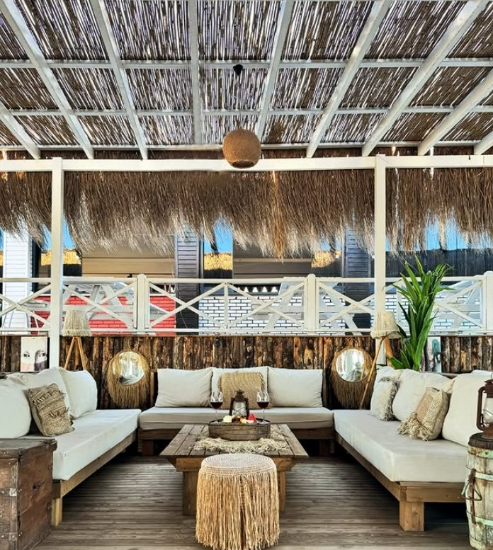 Outdoor tropical lounge with white cushioned sectional, wooden coffee table, and thatched roof.