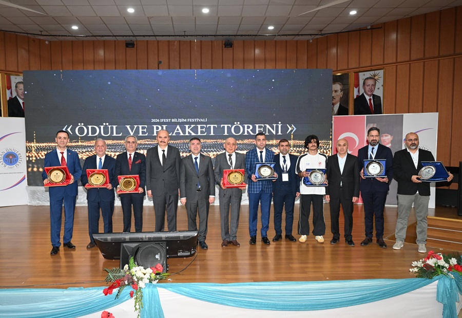 Group of award recipients standing in a row on a stage, each holding circular plaques, with a large banner behind them reading 'ÖDÜL VE PAKET TÖRENİ'.