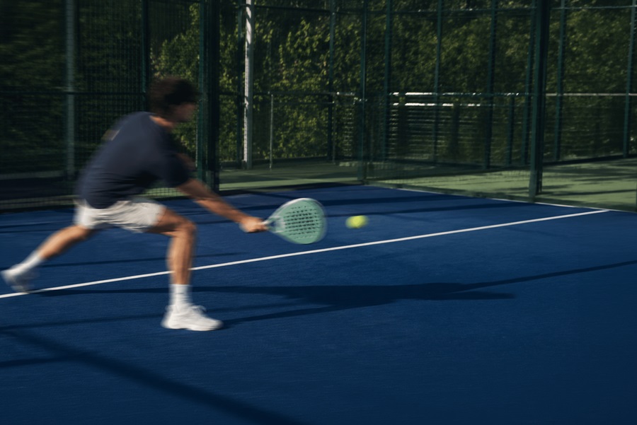 A man on a blue tennis court lunges to hit a yellow tennis ball with a mint-green racket.