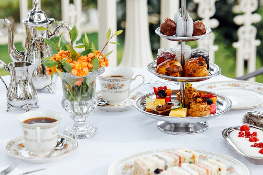 Elegant tea party spread with a three-tiered stand of pastries and macarons on a white tablecloth