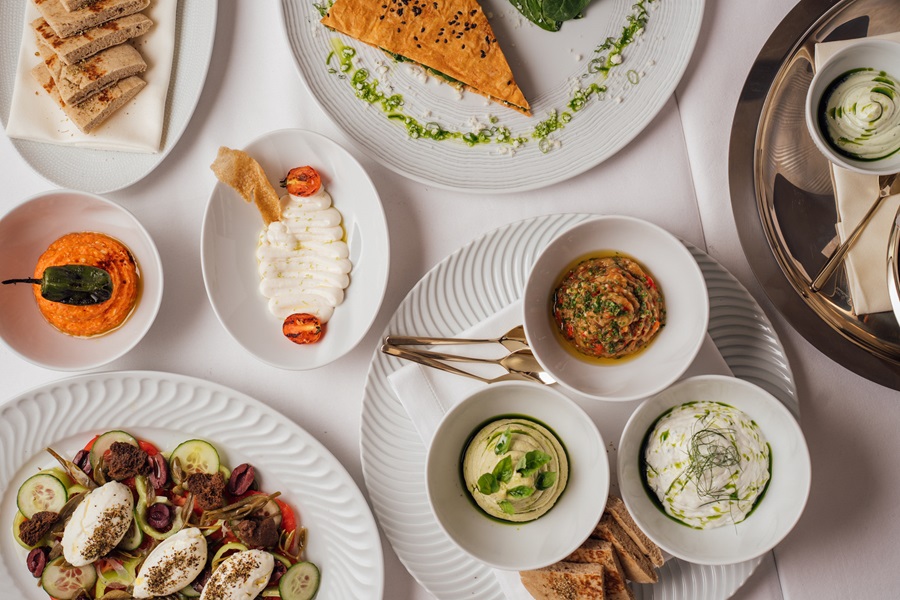 Flat lay of an elegant table with assorted appetizers, breads, salads, and dipping bowls on a white tablecloth.