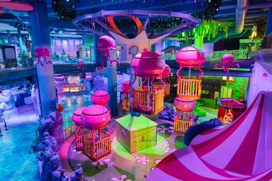 Colorful indoor play area with pink jellyfish-like ride pods and neon lighting for kids' entertainment.
