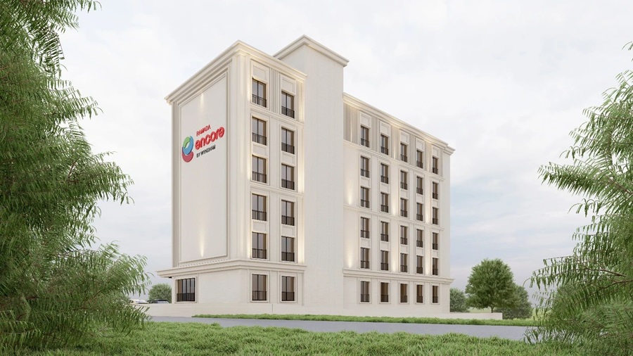 White multi-story modern building with a colorful logo on the left façade, set in a green landscape with palm trees framing the scene.