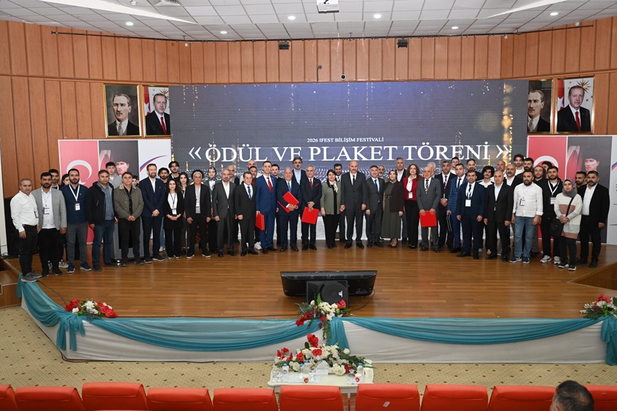 Group of around 50 formally dressed people on a stage posing for a photo after an awards and plaques ceremony, with a large banner reading 'Ödül ve Plaket Töreni' behind them.