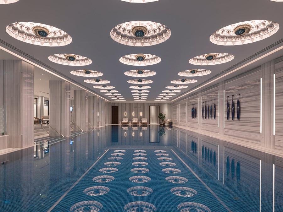 Indoor luxury pool with circular ceiling lamps and marble walls, reflections on the water.