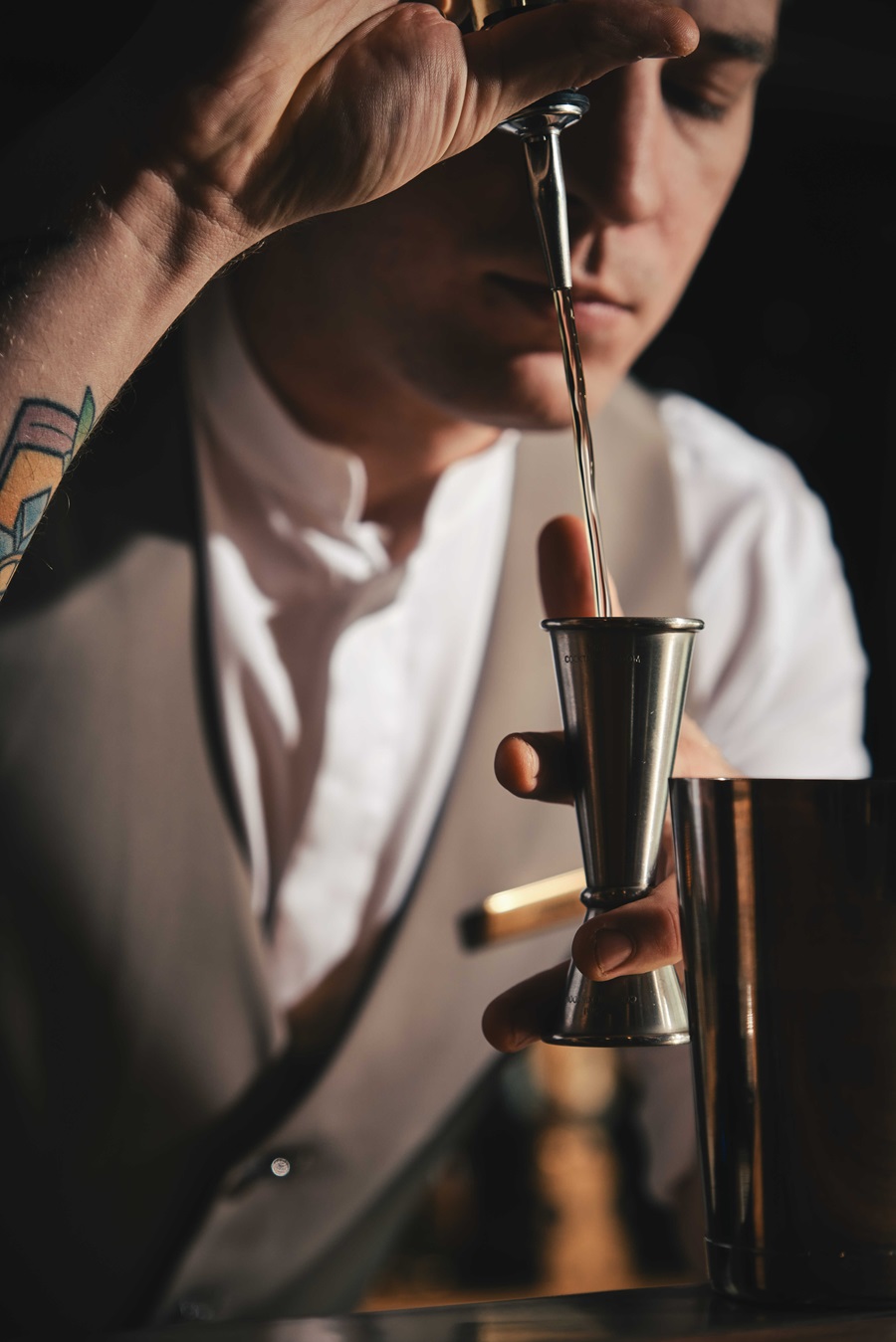 Bartender uses a metal jigger to pour liquid into a shaker for a cocktail.