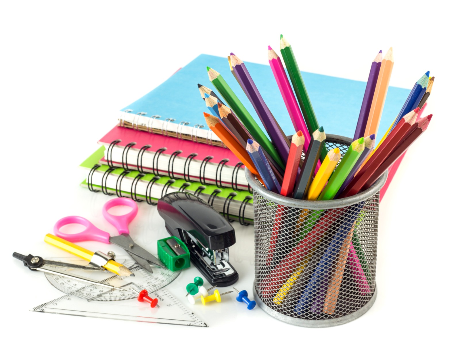 Colorful pencils in a wire mesh cup with spiral notebooks, scissors, and rulers laid out on a white surface—back-to-school supplies.