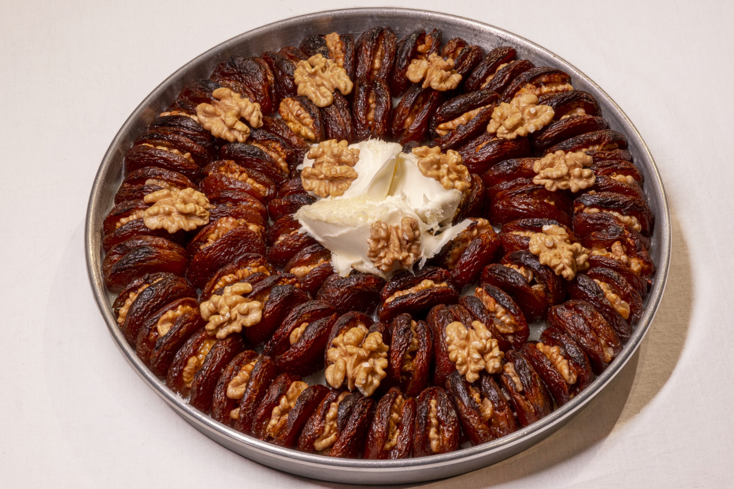 Ring of date-wuen cookies layered with walnut halves around a central scoop of cream cheese on a round metal serving tray.