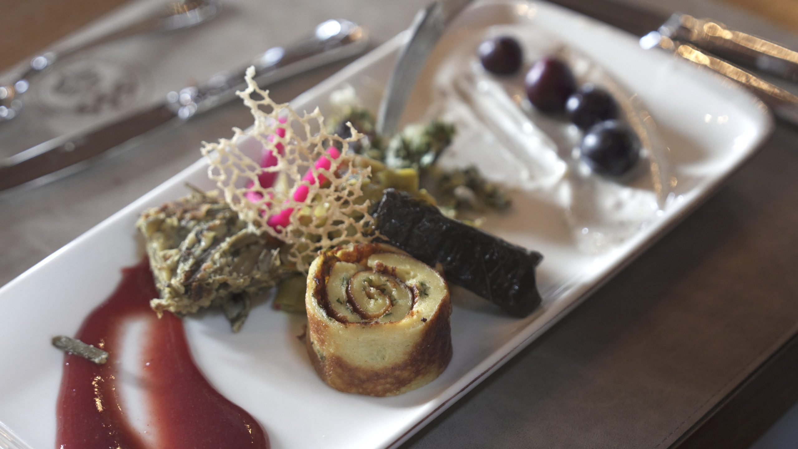 Plate of gourmet appetizers featuring a rolled savory pastry, a crispy lattice garnish, and a dark glaze on the side.