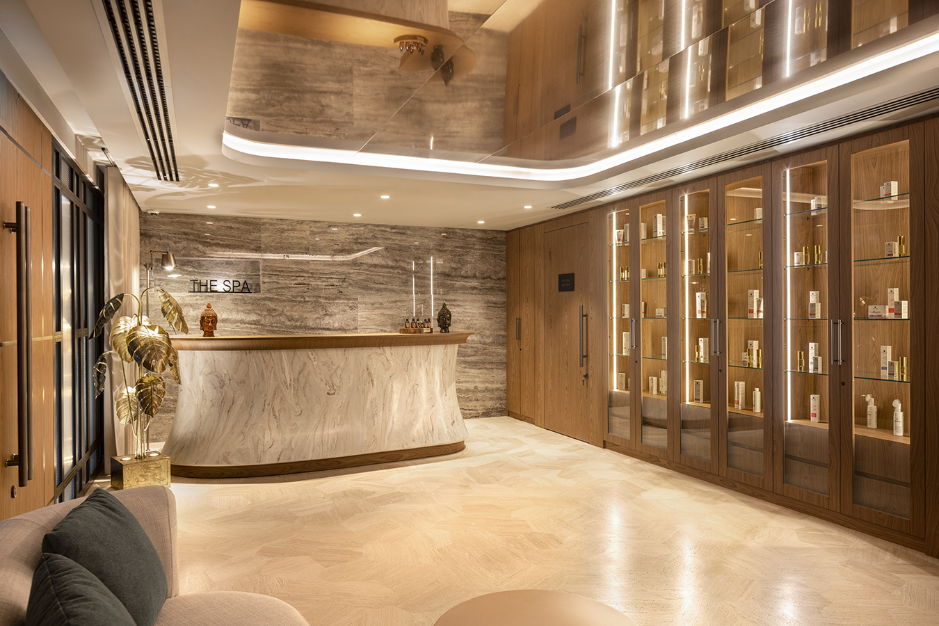 Luxurious spa reception with a curved marble desk, warm lighting, and glass-front product shelves along the wall.