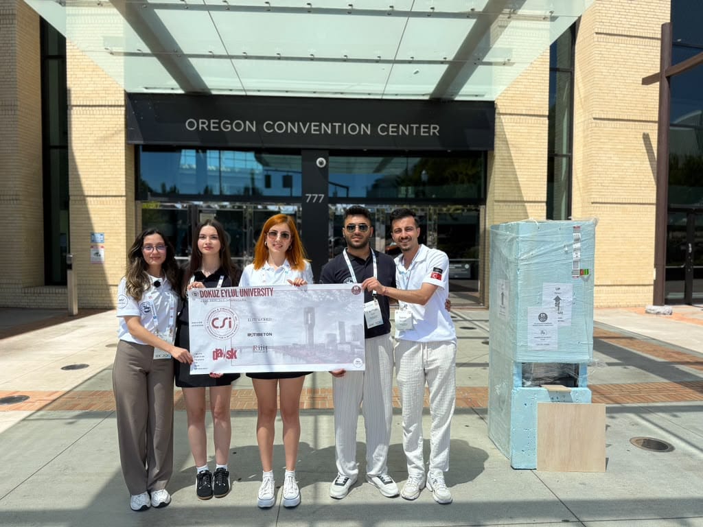 Five young adults stand outside the Oregon Convention Center, holding a large banner for Dokuz Eylül University.